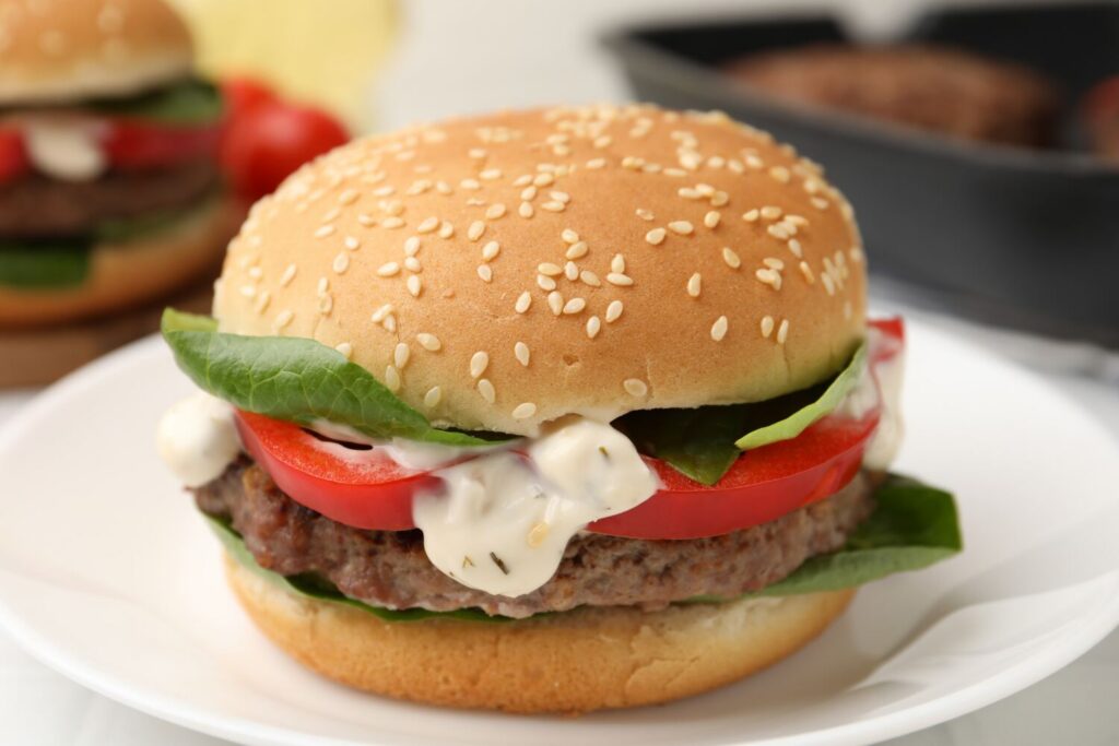 Delicious burger with meat patty on white table, closeup